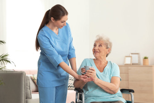 A caregiver giving cup of tea of an elderly woman in wheelchair