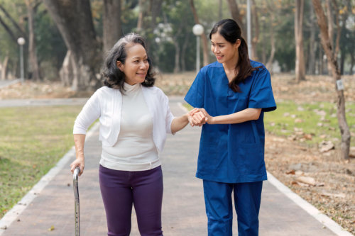 female caregiver assisting a elderly woman to walk in outdoors
