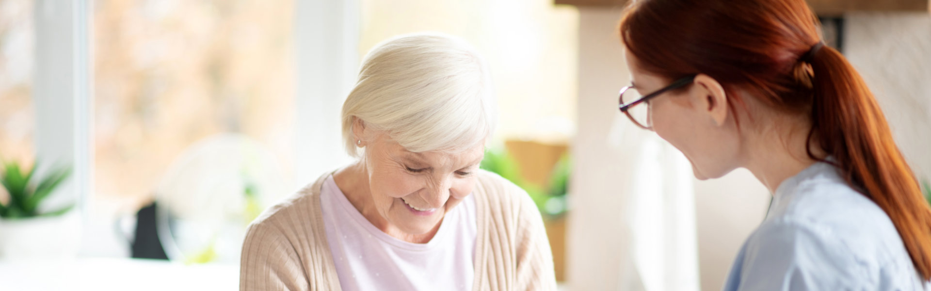 Elderly woman smiling as a healthcare worker assists her in organizing daily medication with a pill organizer at home